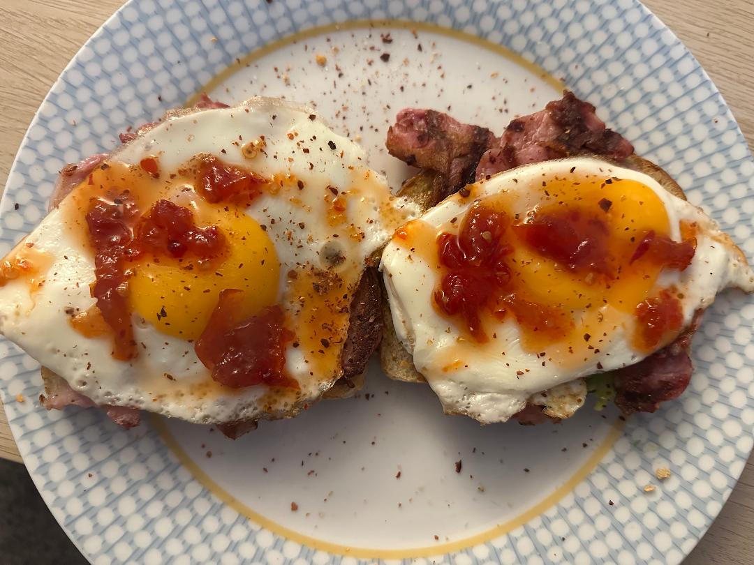 Two fried eggs with Original Chilli Relish (chilli jam) on top of bacon rolls on a plate with a blue and white pattern.