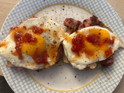 Two fried eggs with Original Chilli Relish (chilli jam) on top of bacon rolls on a plate with a blue and white pattern.
