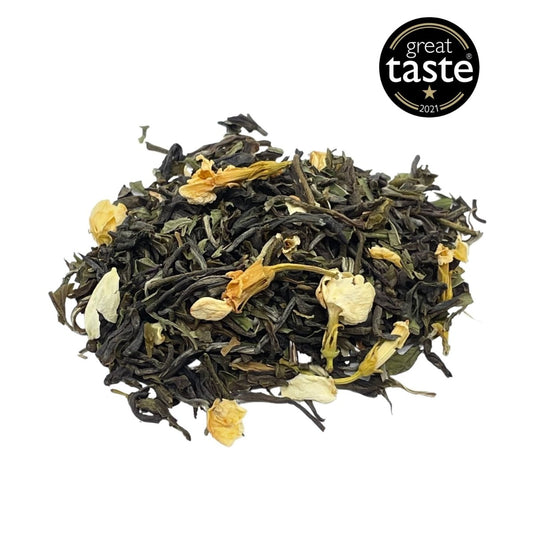Loose leaf Jasmine and Mint Green Tea from Camellios in a clear glass jar with fresh tea leaves and herbs inside.