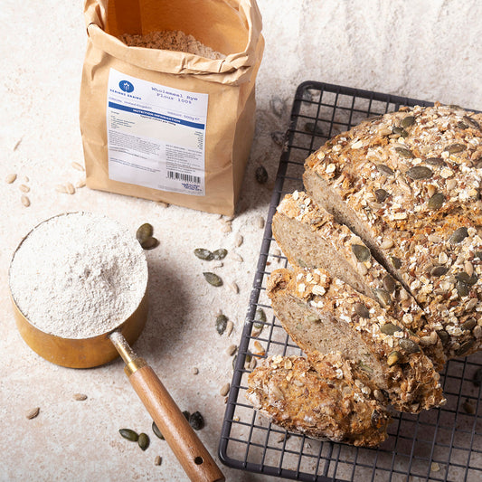 Wholemeal rye flour in a bag from Serious Grains by Whole Food Earth, displayed on a rustic wooden surface with baking ingredients.