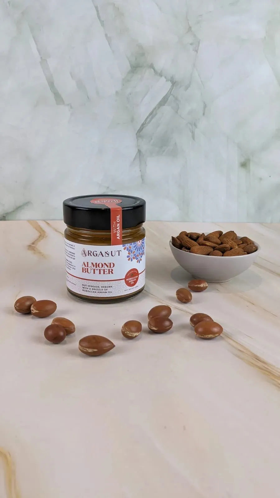 Creamy almond butter with argan oil on marble surface, showcasing smooth texture and natural nut butter appearance.
