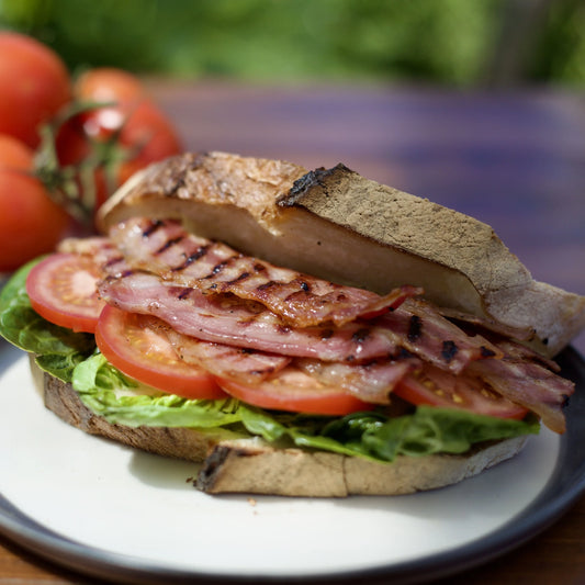 Sliced smoked back bacon from Primrose Herd, dry cured, displayed in a bacon bap sandwich with fresh bread and toppings.