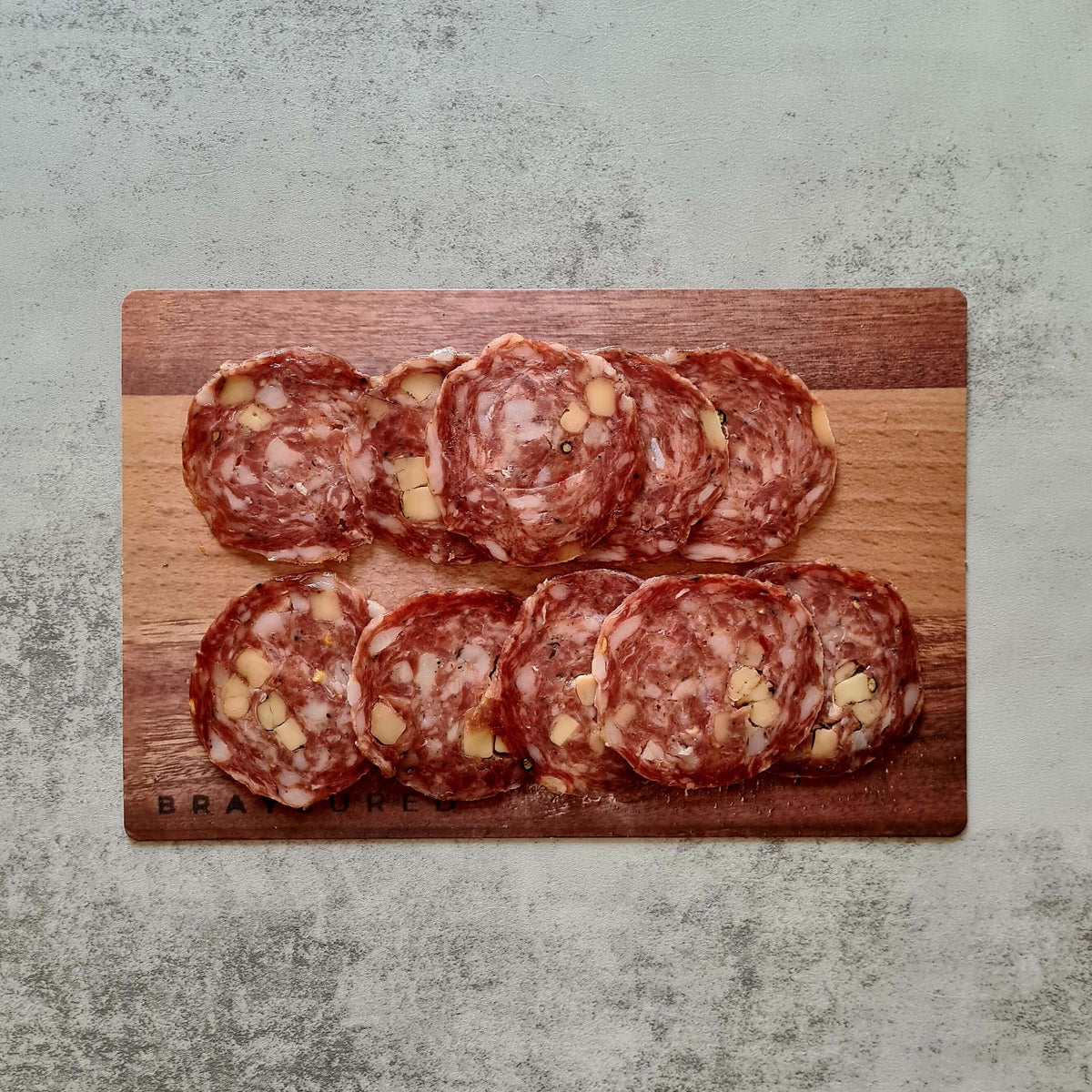 Thin slices of Bray Cured Berkshire Salami on a charcuterie board with cheese, nuts, and crackers, ready for serving.