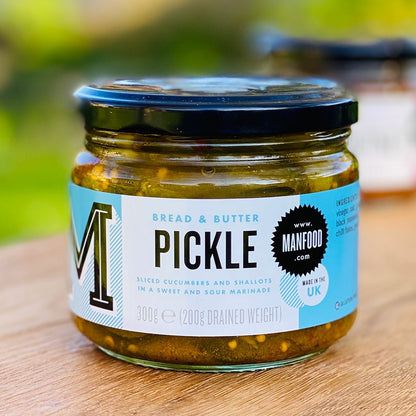 Jar of Manfood bread and butter pickles with sliced cucumbers and spices in a clear glass jar.