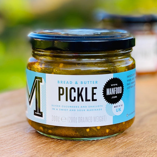 Jar of Manfood bread and butter pickles with sliced cucumbers and spices in a clear glass jar.