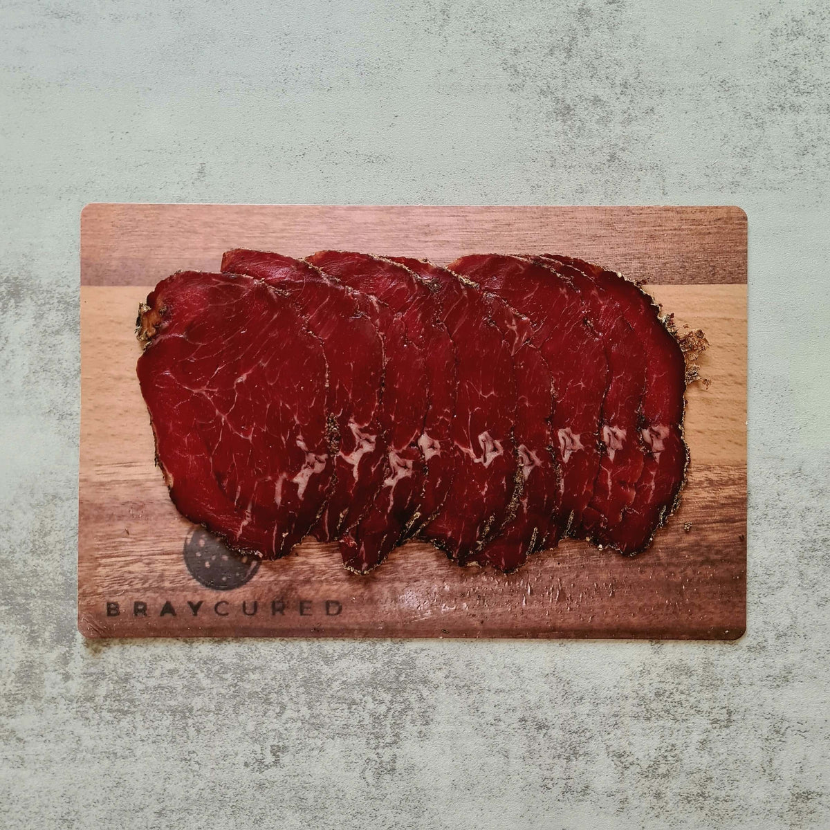 Thin slices of Bray Cured Classic Bresaola beef charcuterie on a wooden board with fresh herbs and accompaniments.