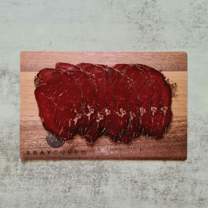 Thin slices of Bray Cured Classic Bresaola beef charcuterie on a wooden board with fresh herbs and accompaniments.