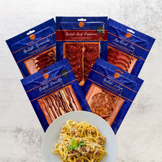 Assorted British charcuterie meats from Bray Cured, ideal for pasta dishes, displayed on a wooden board with herbs and cheese.