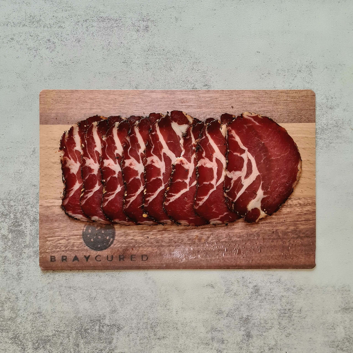 Thinly sliced Air-Dried Coppa from Bray Cured on a wooden charcuterie board, showcasing rich marbling and deep red color.