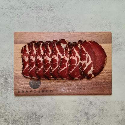 Thinly sliced Air-Dried Coppa from Bray Cured on a wooden charcuterie board, showcasing rich marbling and deep red color.