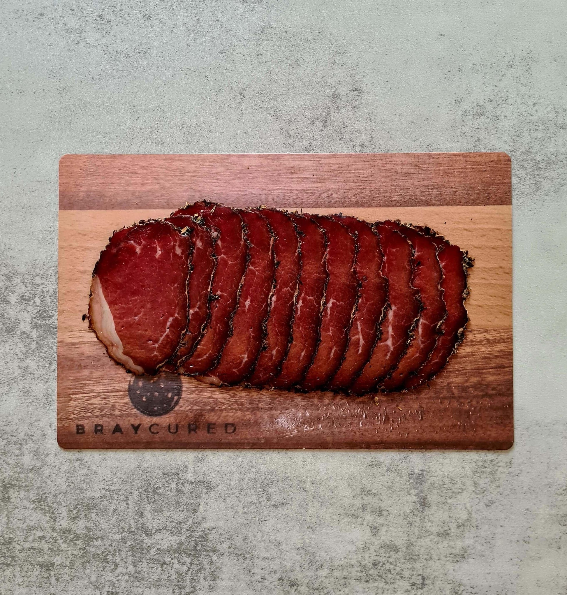 Thin slices of Bray Cured Hogget Bresaola arranged on a charcuterie board with herbs and accompaniments for a savory presentation.
