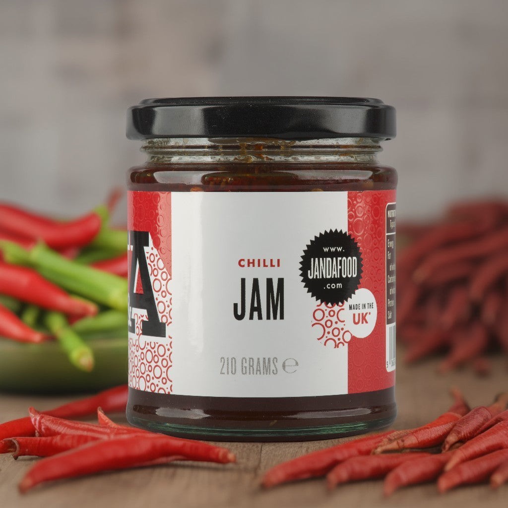 Janda Food Chilli Jam in a glass jar surrounded by fresh red chillies on a wooden surface