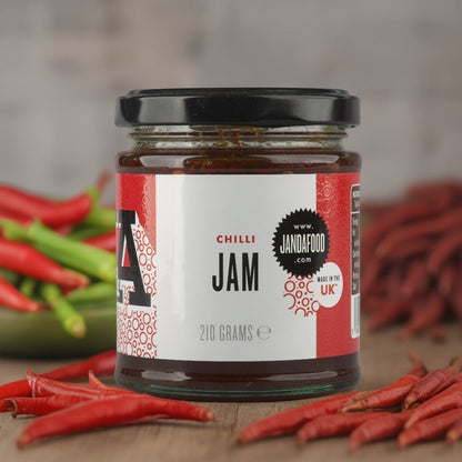 Janda Food Chilli Jam in a glass jar surrounded by fresh red chillies on a wooden surface