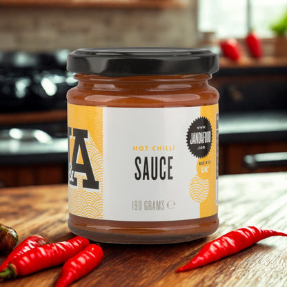 Janda Food hot chilli sauce in a glass jar with red jalapeno and habanero chillies on a wooden kitchen table