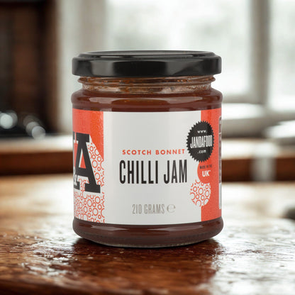 Janda Scotch Bonnet Chilli Jam jar showing the label, with a spoon of bright red spicy-sweet chili jam beside it.