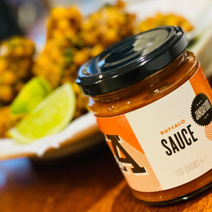Janda Food vegan buffalo sauce in a glass jar with orange label, served with crispy cauliflower and lime wedges.
