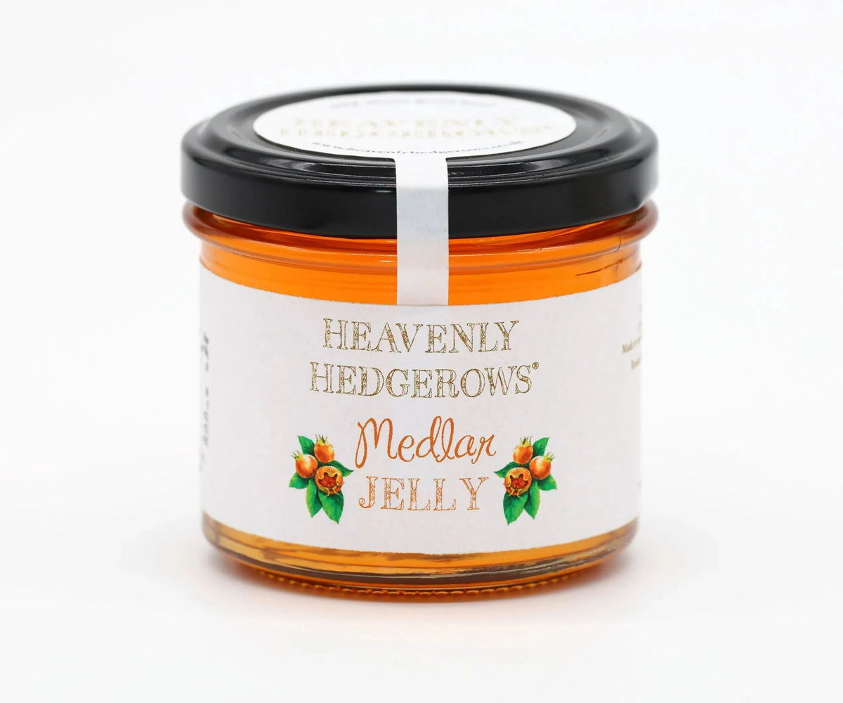 Jar of Heavenly Hedgerows medlar jelly with a spoon and fresh medlar fruit on a rustic wooden surface.