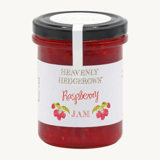 Jar of Heavenly Hedgerows raspberry jam with fresh raspberries and a rustic wooden background.