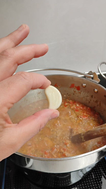 Hand holding a clove of garlic above a pot of chilli condiment