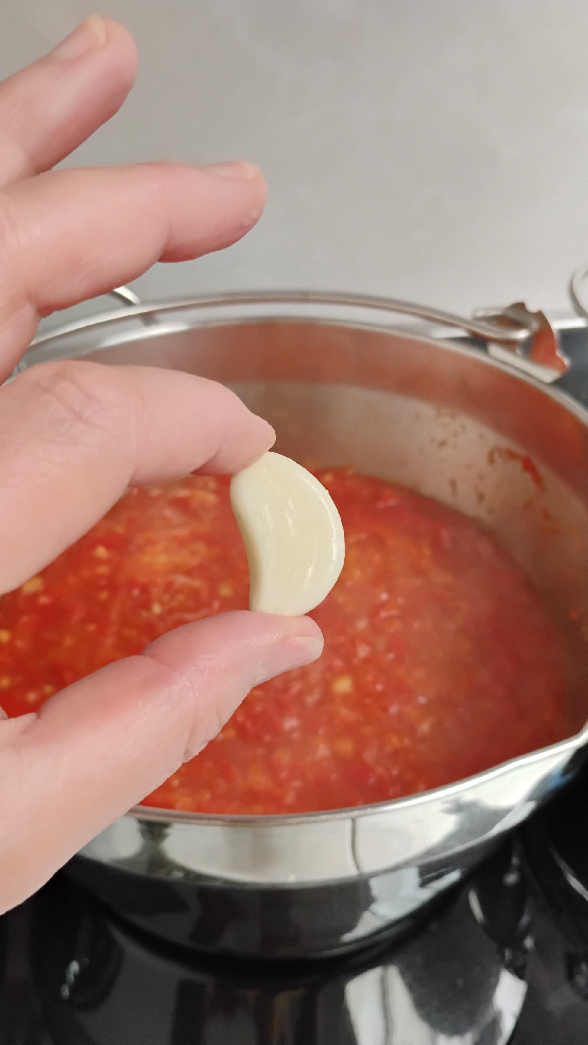 Hand holding a garlic clove above a pot of chilli jam.