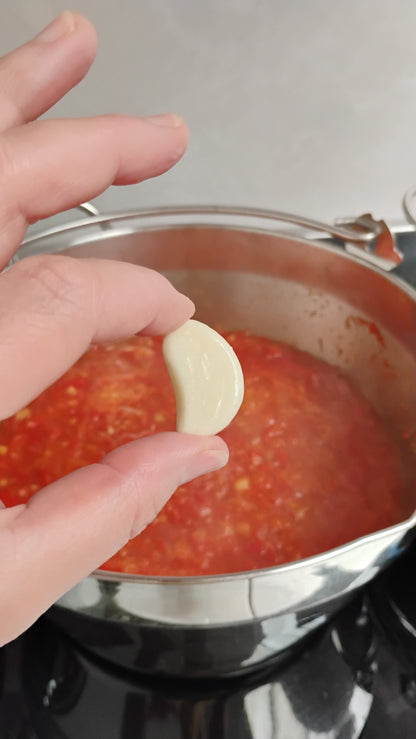 Hand holding a garlic clove above a pot of chilli jam.