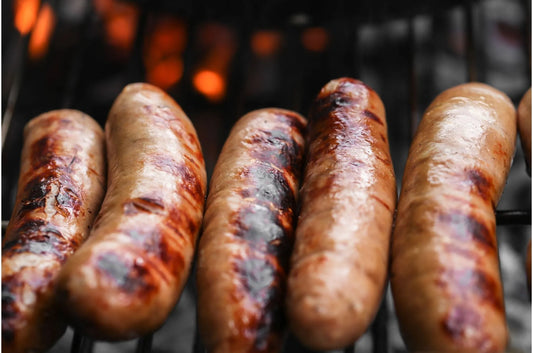 Primrose Herd sage and red onion sausages, cooked and plated on a white dish with fresh herbs and red onion slices visible.