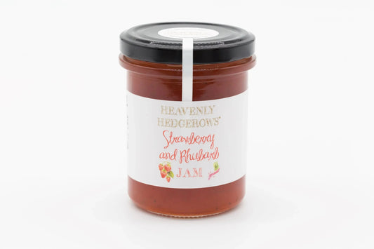 Heavenly Hedgerows strawberry and rhubarb jam in a glass jar with fresh fruit and rhubarb stalks on a rustic background.