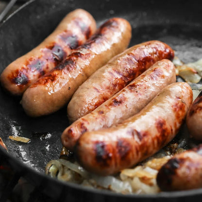 Primrose Herd gluten-free pork sausages cooking in a pan, showcasing their golden-brown exterior and appetizing appearance.