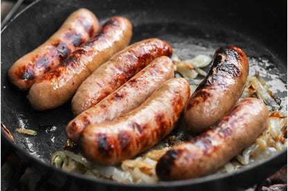 Primrose Herd pork and garlic sausages cooking in a pan, showing crispy golden-brown exterior and juicy interior.