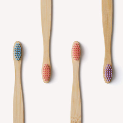 Four colorful children's bamboo toothbrushes from Wild And Stone in candy colors, featuring soft bristle heads suitable for kids.