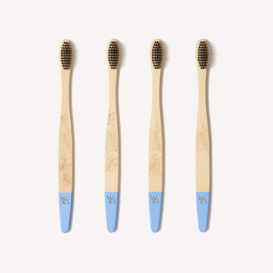 Four adult bamboo toothbrushes with firm bristles from Wild and Stone, featuring natural bamboo handles.