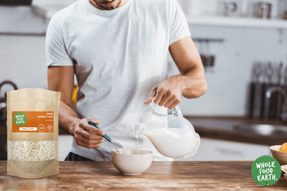 Raw organic buckwheat flakes from Whole Food Earth, gluten-free cereal in a clear bowl with a spoon on a wooden surface.