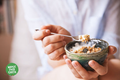 Organic Deluxe Muesli by Whole Food Earth featuring a mix of flakes, nuts, seeds, and dried fruit in a cereal bowl.