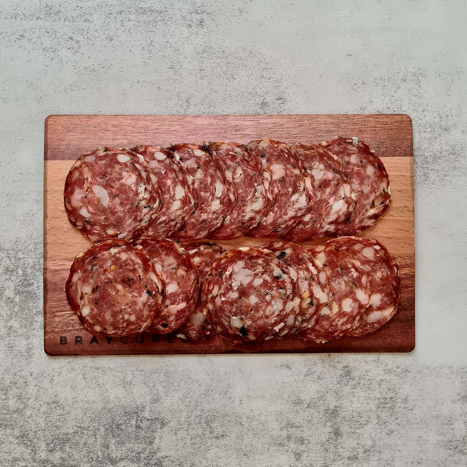 Thinly sliced Bray Cured personal salami with wild garlic, arranged on a charcuterie board featuring cheese, nuts, and fresh herbs.