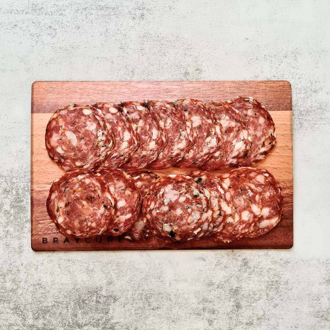 Slices of Bray Cured Wild Garlic Salami on a charcuterie board with crackers and herbs, showcasing the artisanal cured meat.