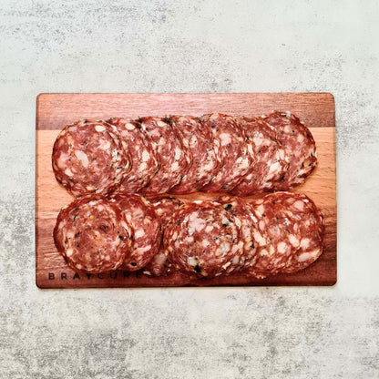Slices of Bray Cured Wild Garlic Salami on a charcuterie board with crackers and herbs, showcasing the artisanal cured meat.